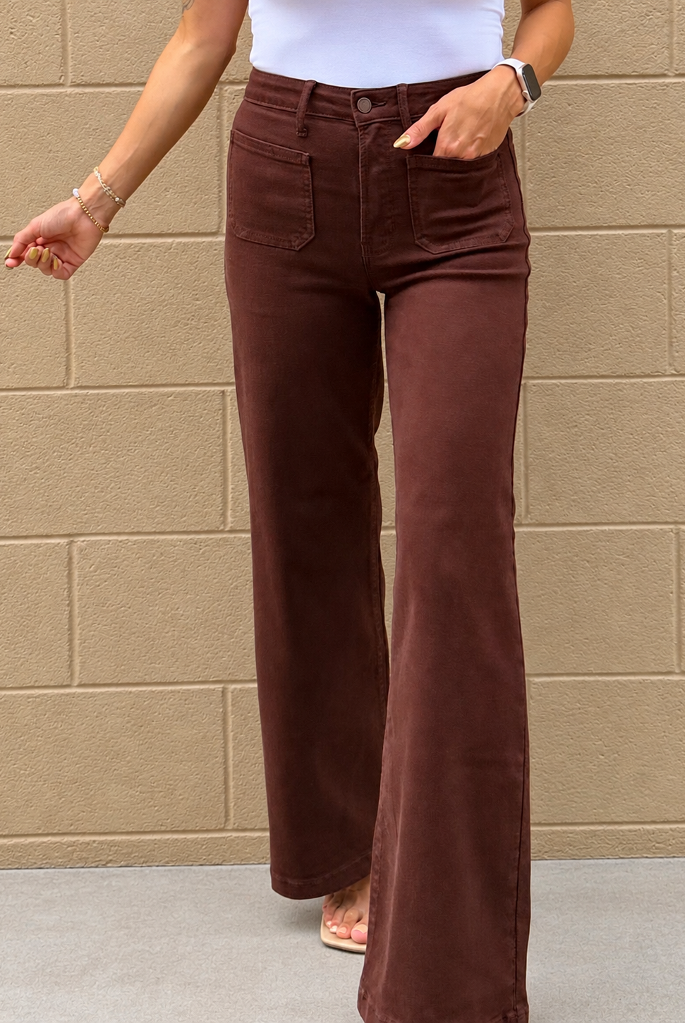 A person wearing dark brown wide-leg corduroy pants, standing against a beige brick wall.