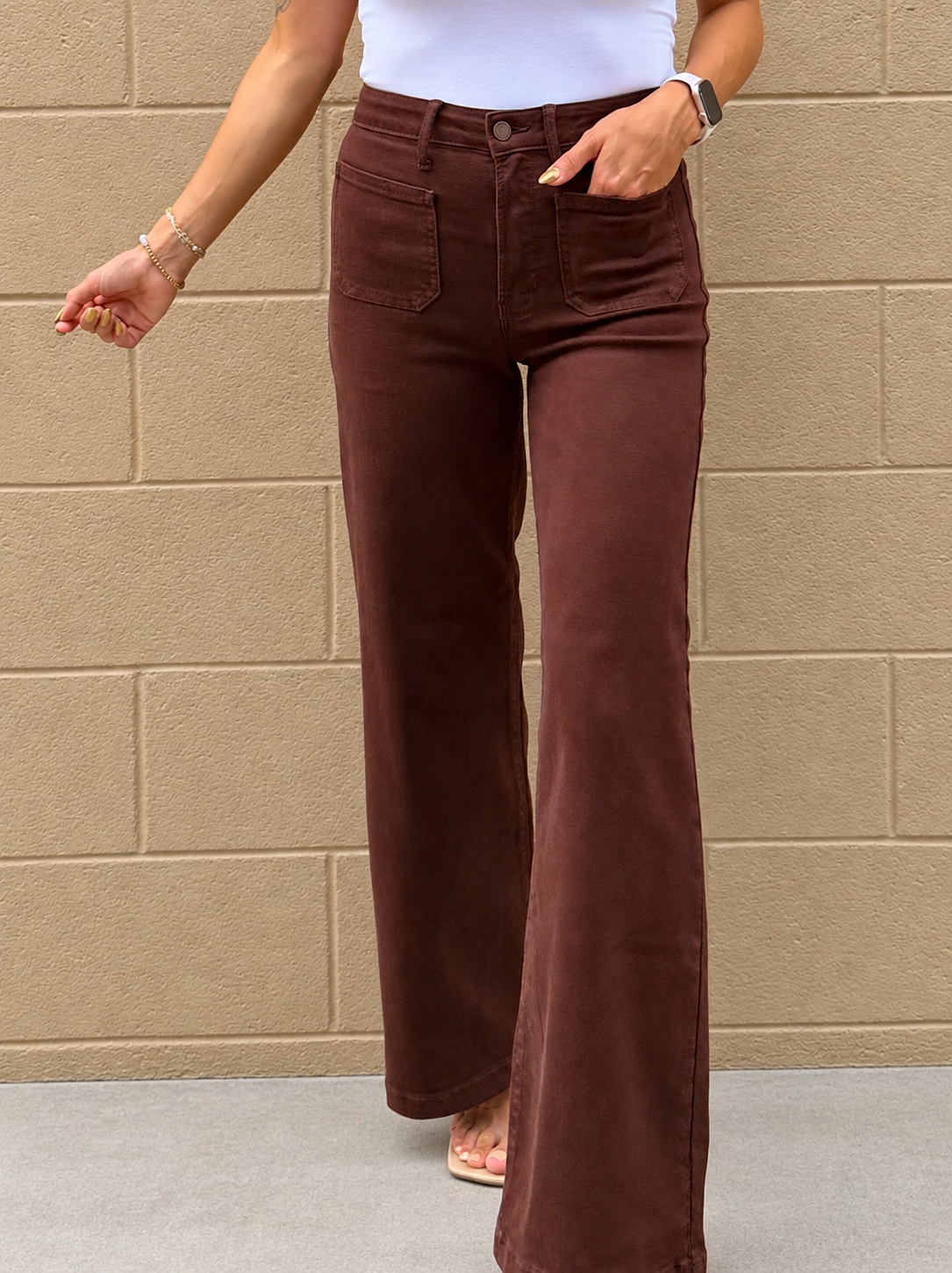 A person wearing dark brown wide-leg corduroy pants, standing against a beige brick wall.